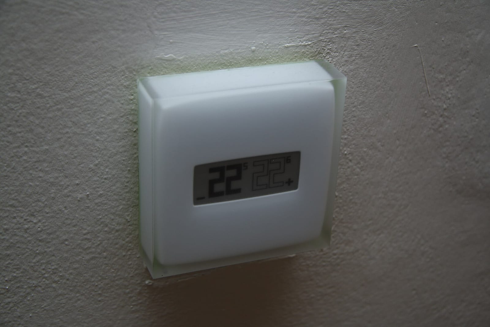 A smart thermostat mounted on a wall showing the room temperature