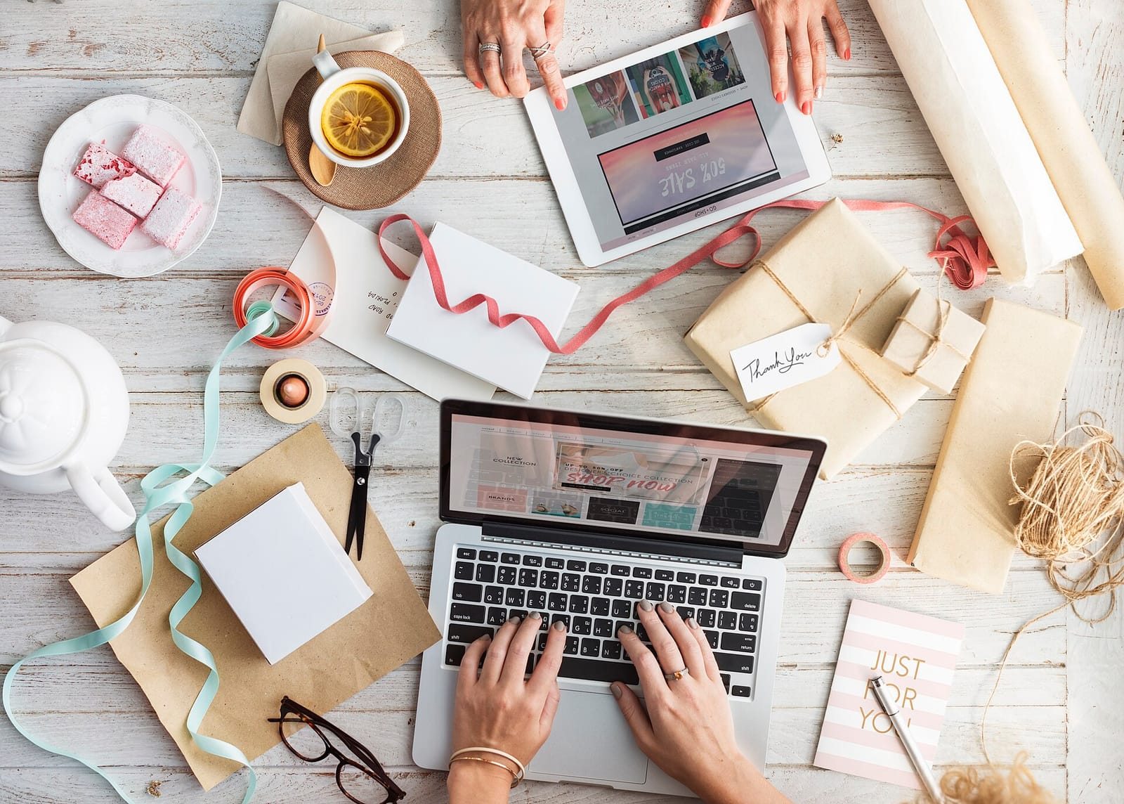 Hands typing on a laptop beside gift wrapping, parcels and a tablet on a wooden table