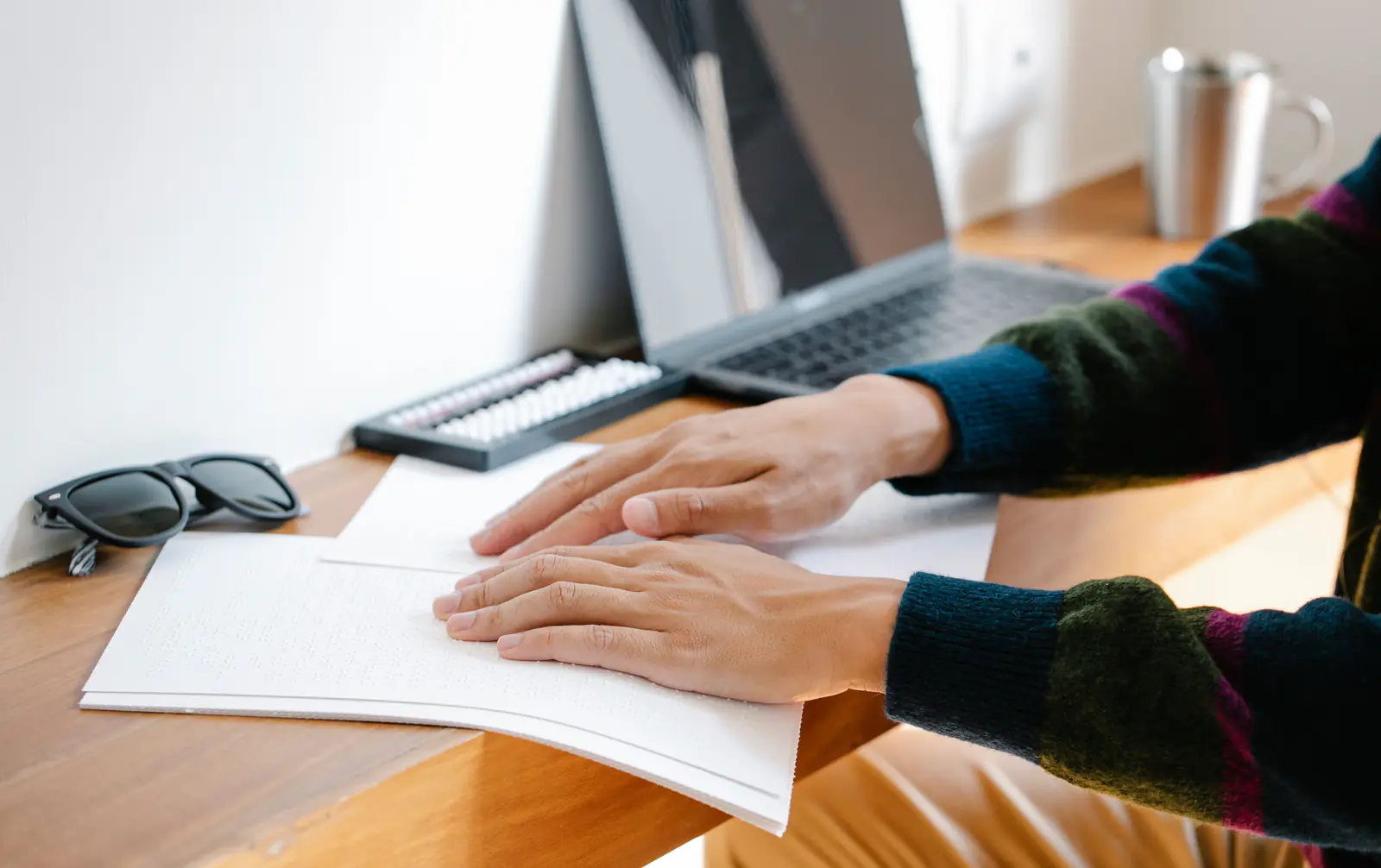 Close-up of hands reading braille at a desk