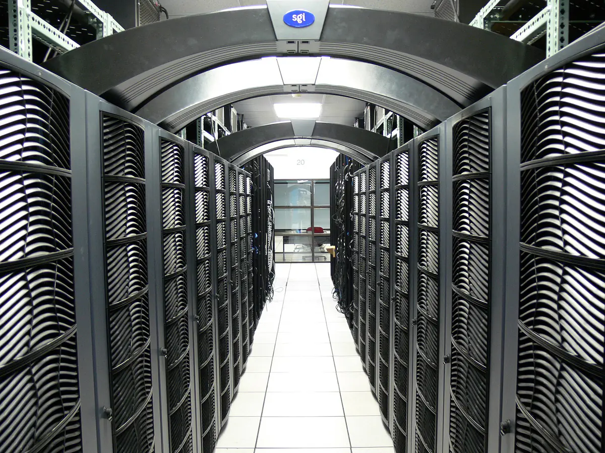 A narrow aisle between tall black server cabinets in a computing hall