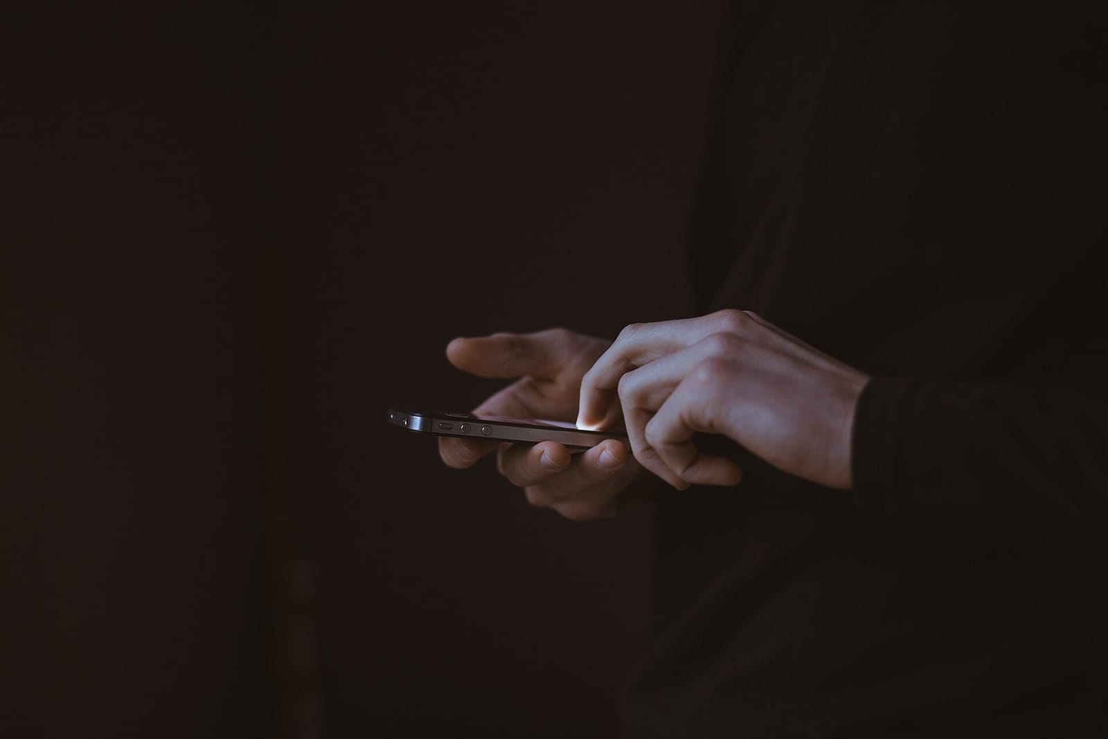 Hands holding a lit smartphone in a dark room