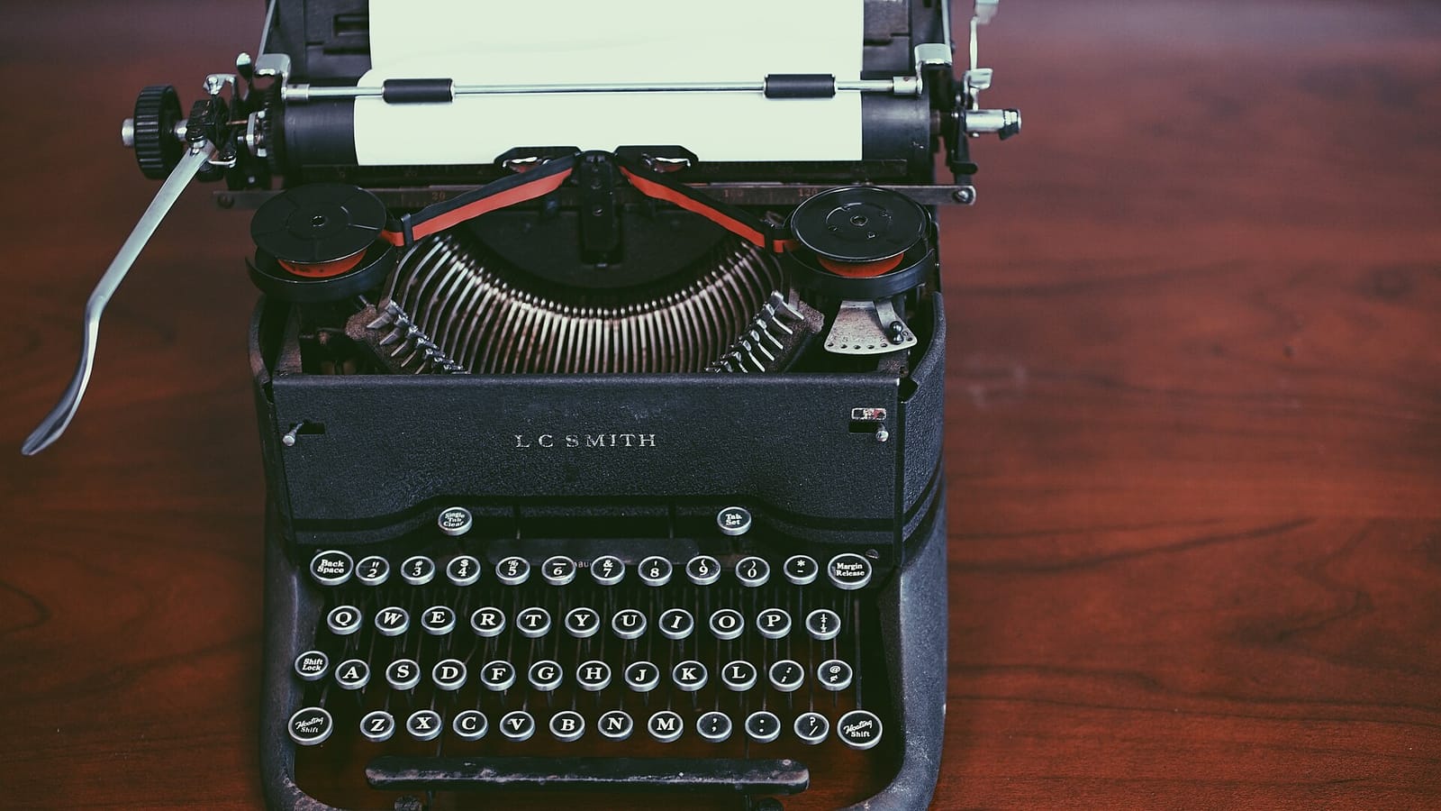 A vintage black L.C. Smith typewriter with a sheet of paper on a wooden desk