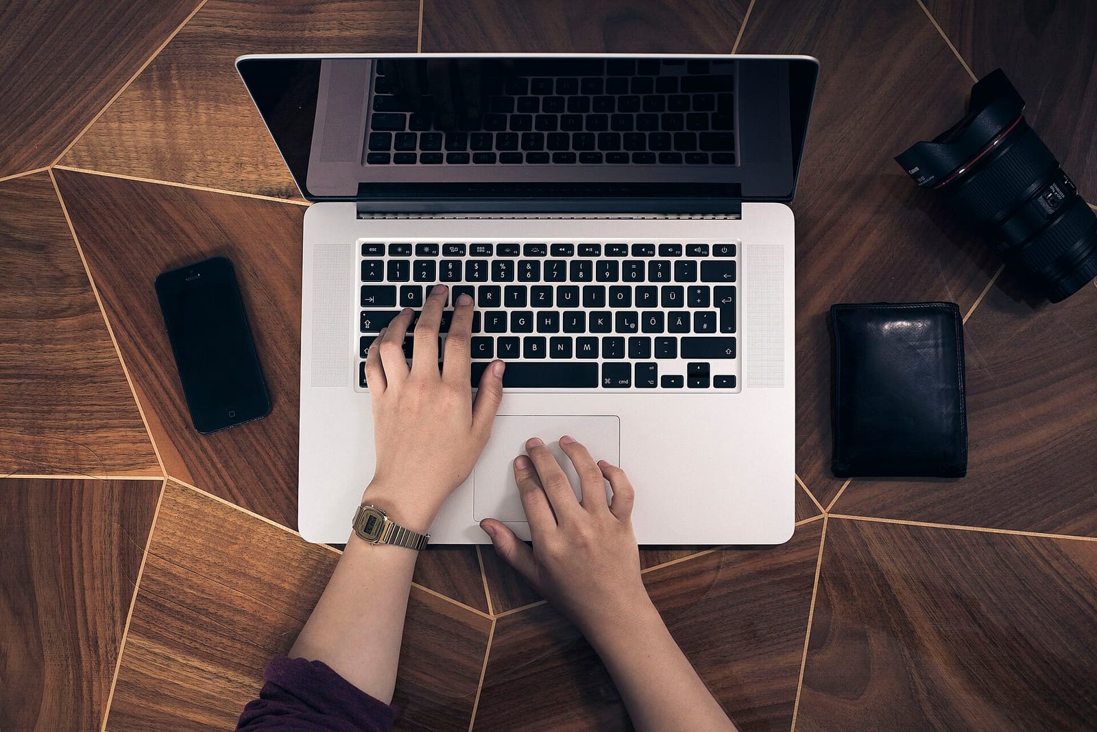 Overhead view of hands typing on a laptop on a wooden desk