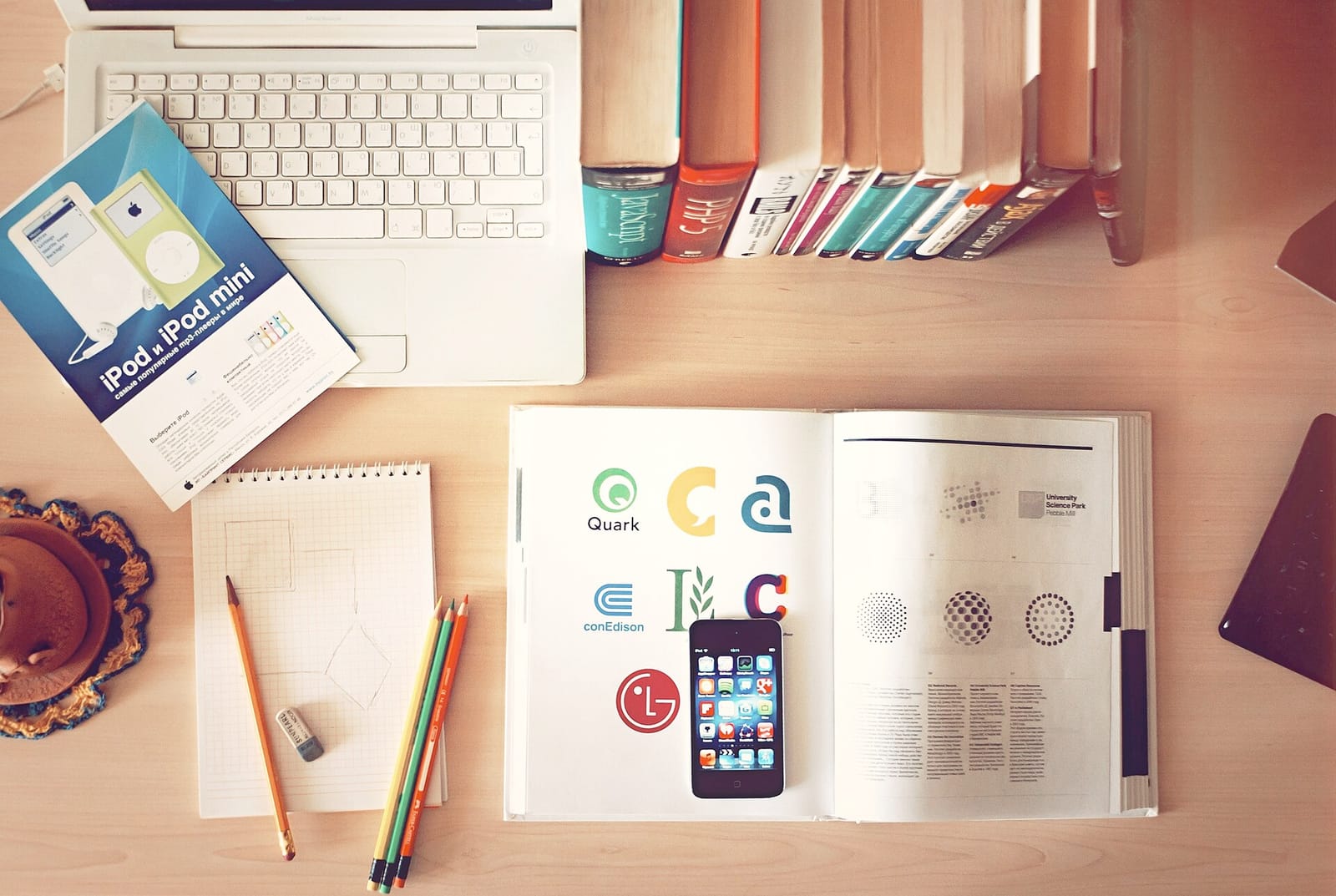 A desk with a laptop, books, notebooks, pencils and a smartphone