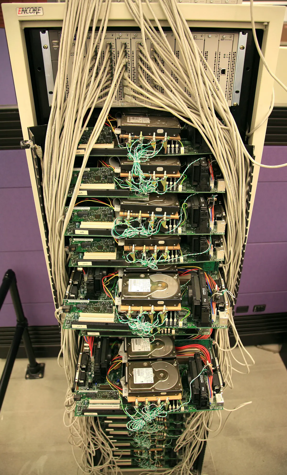 An open rack of bare PC motherboards and hard drives with bundles of network cables, displayed in a museum