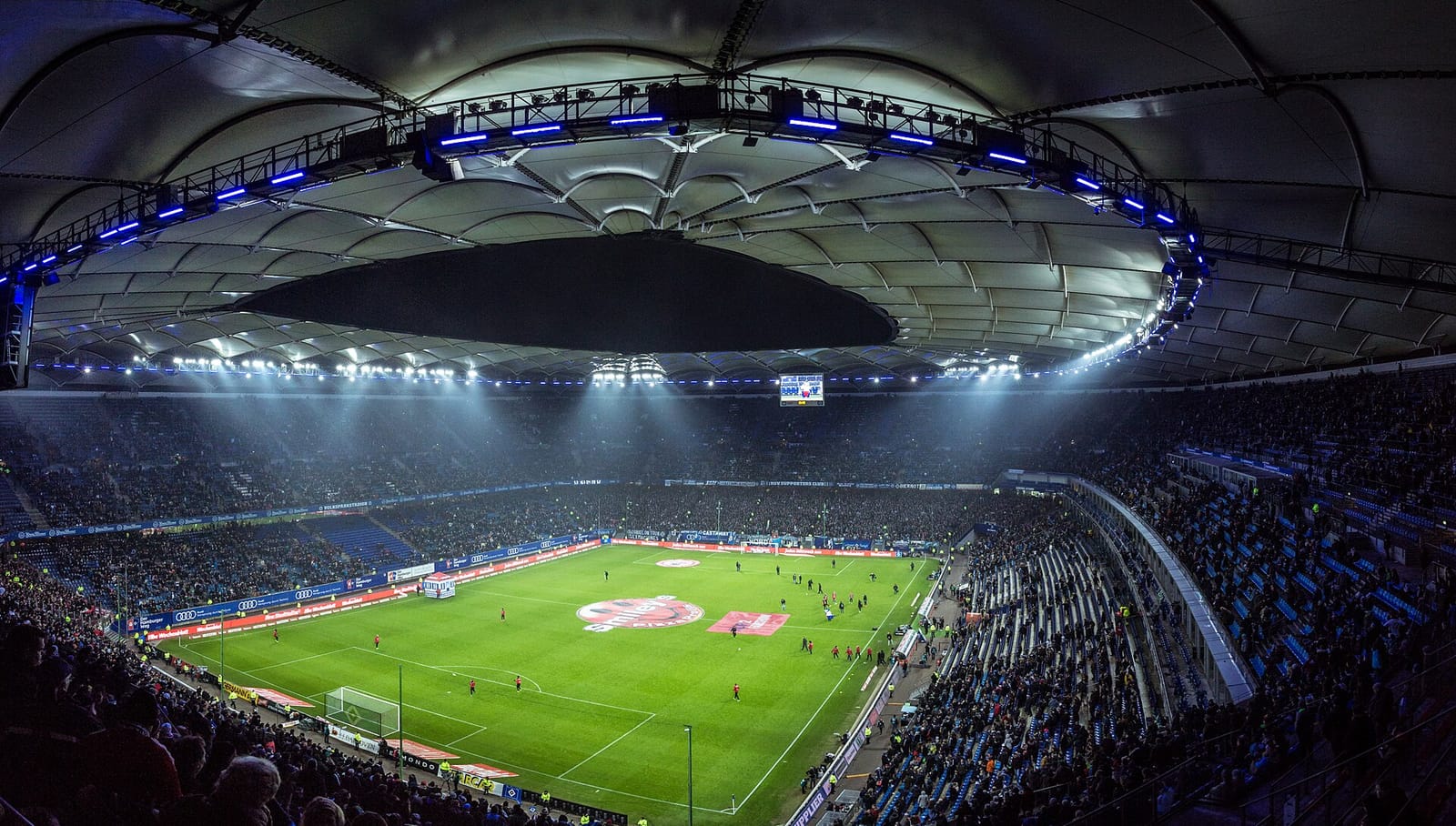A floodlit football stadium full of spectators during a match