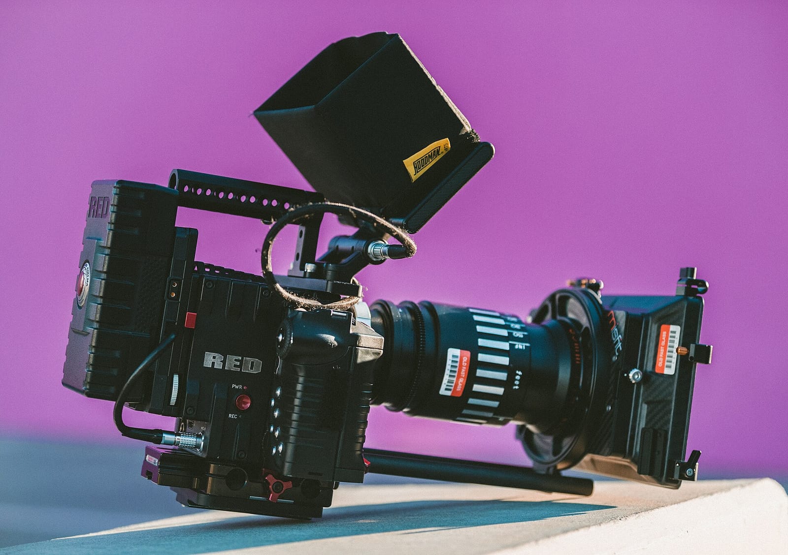 A RED digital cinema camera with a matte box against a pink background