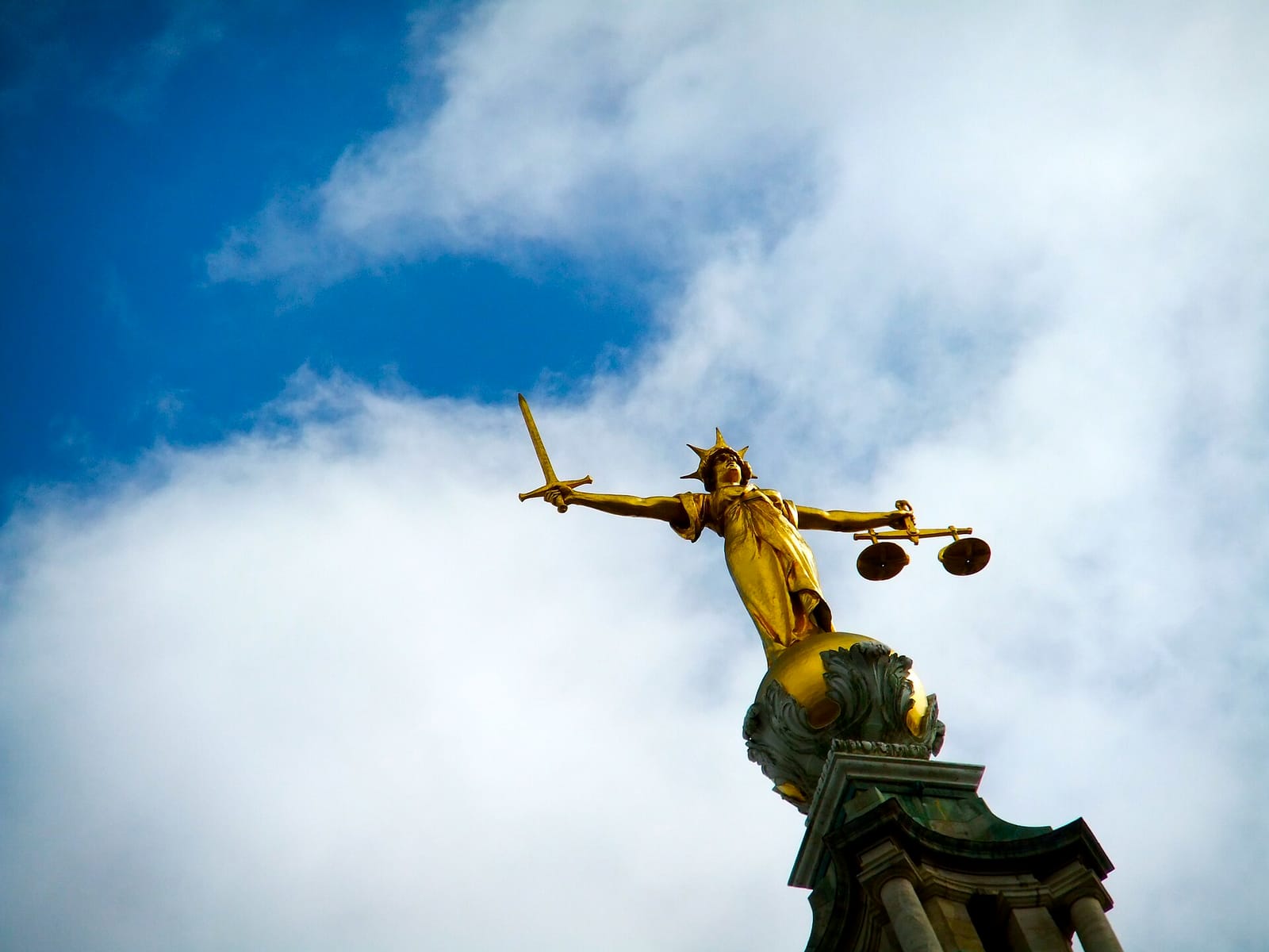 Gilded statue of Lady Justice holding scales against a blue sky