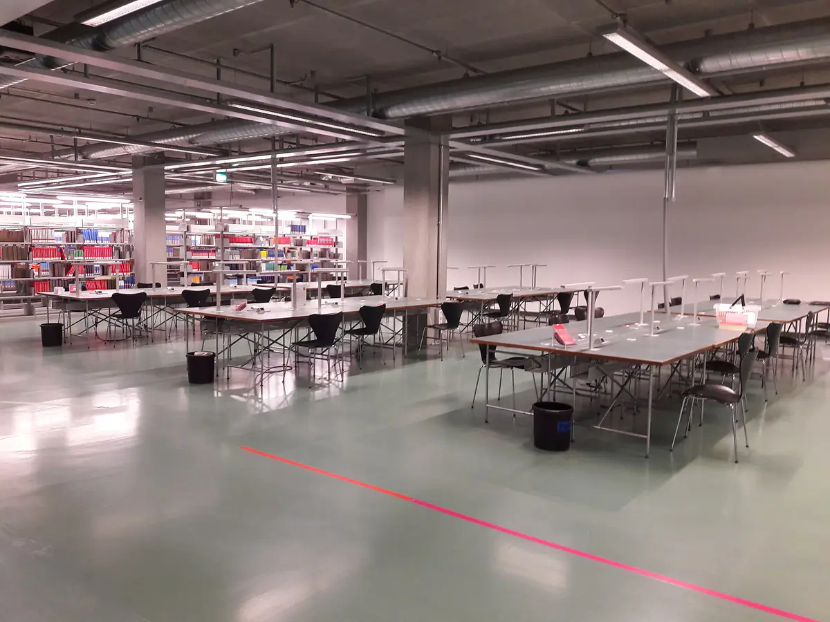 Long study tables and chairs in a university library reading room, with bookshelves behind