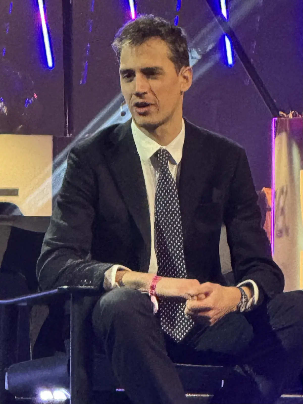 Arthur Mensch in a dark suit and tie, seated on stage at a conference