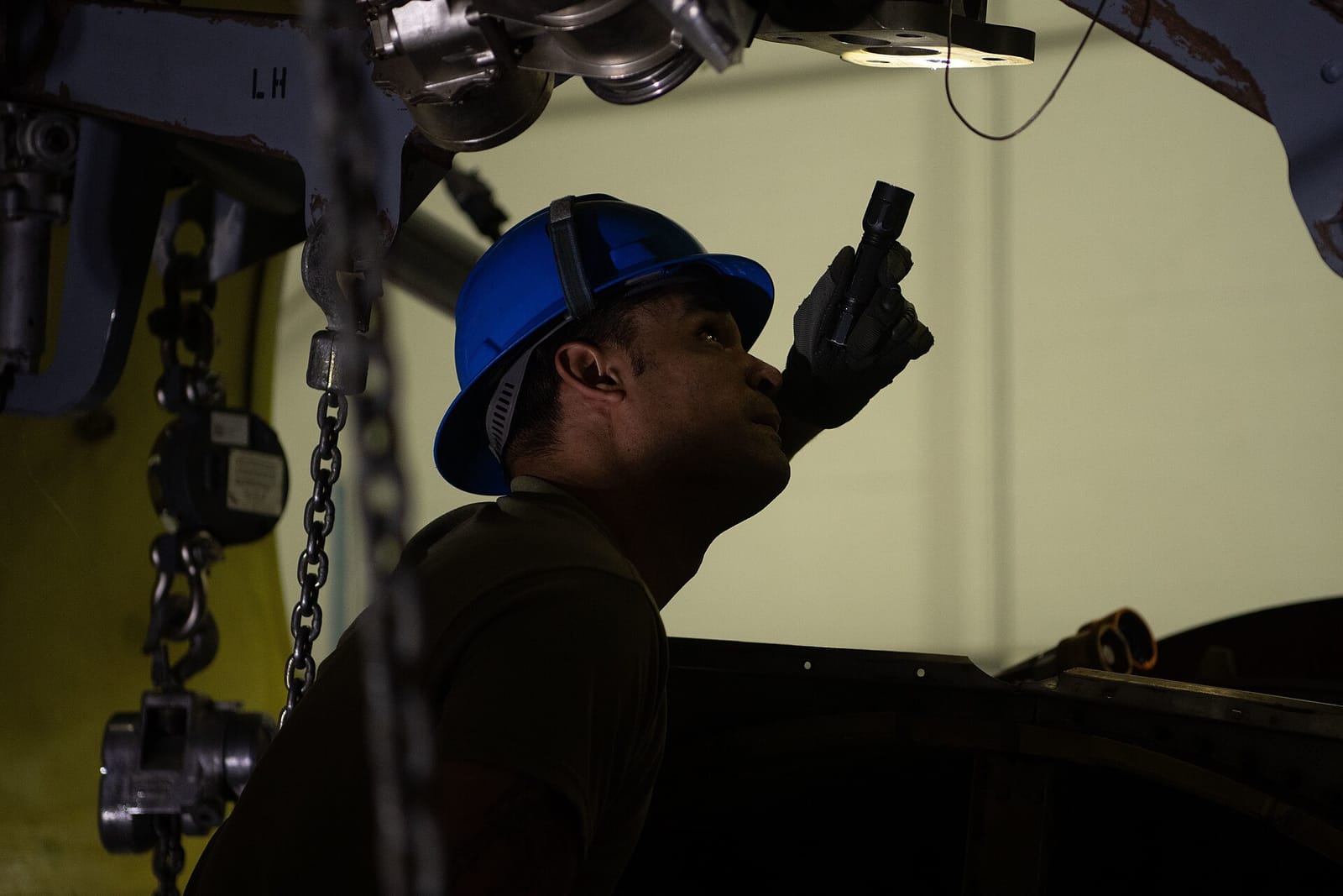 A maintenance technician in a hard hat inspecting an aircraft engine mount with a flashlight