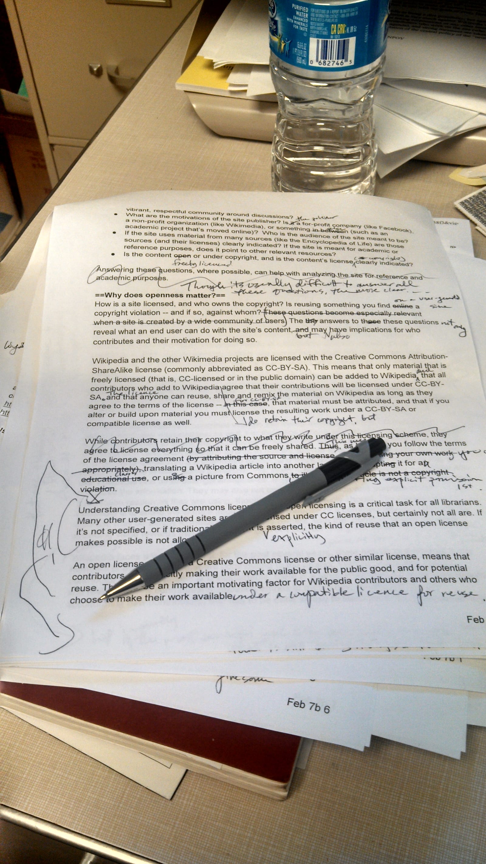Printed manuscript pages covered in handwritten editing marks, with a pen on top