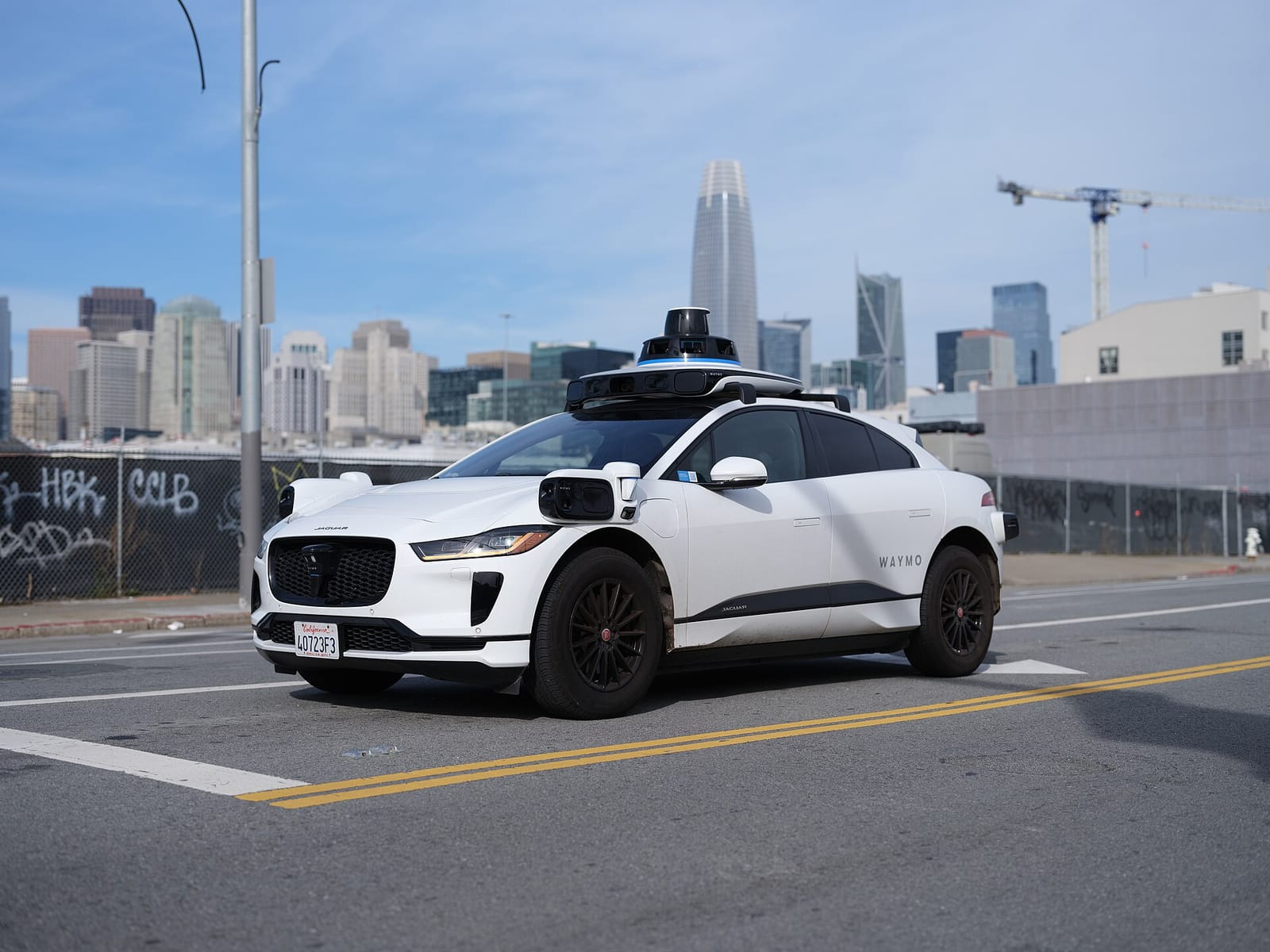 A Waymo self-driving Jaguar I-Pace with roof-mounted sensors on a street in San Francisco