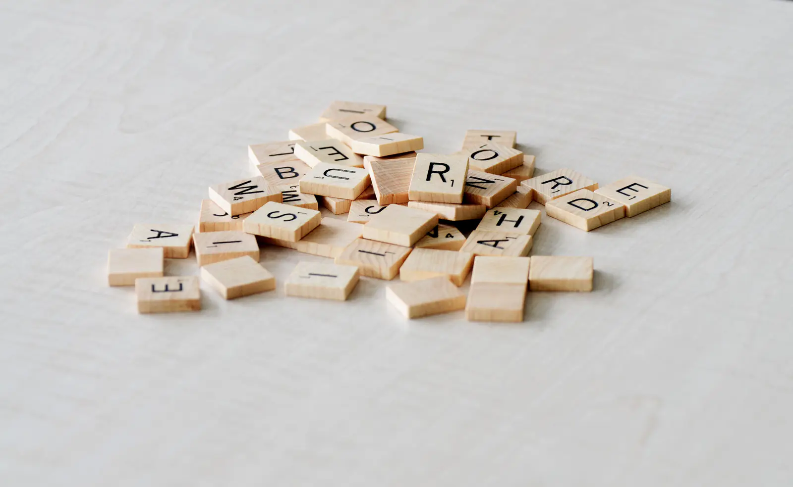 A pile of wooden letter tiles scattered on a light surface