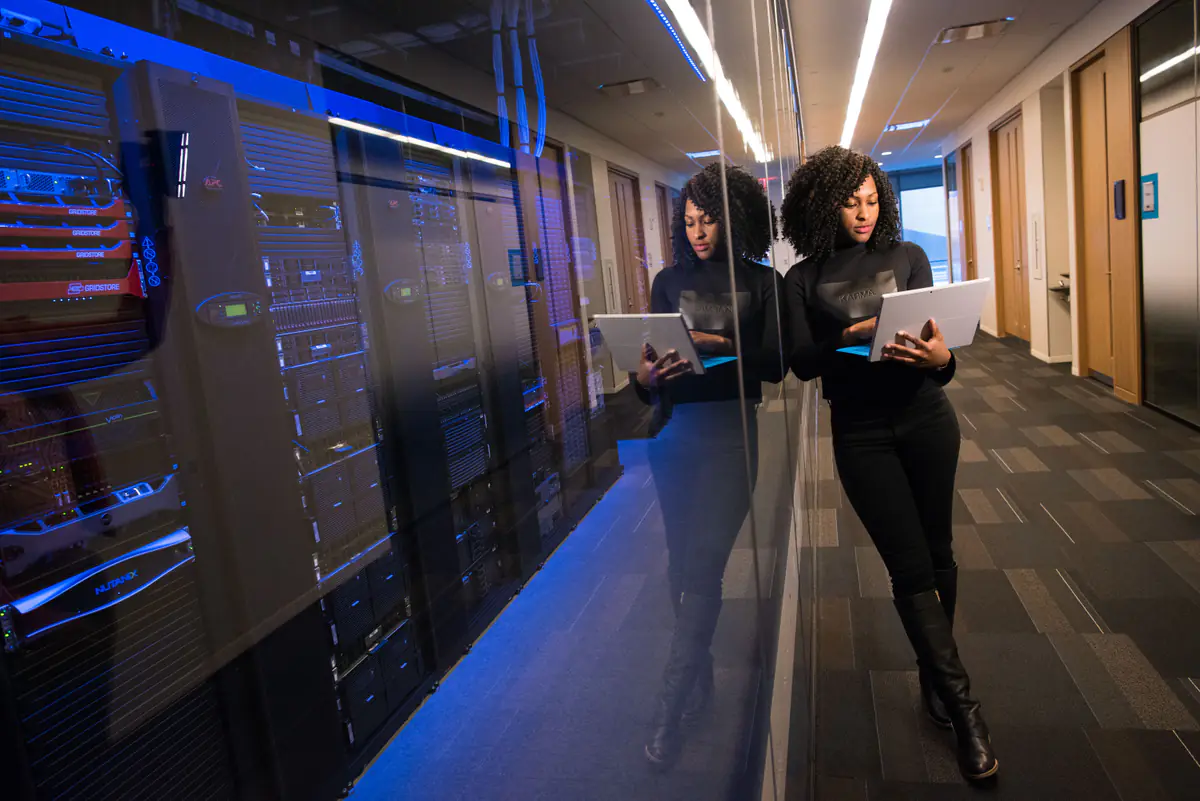 A woman holding a laptop among server racks