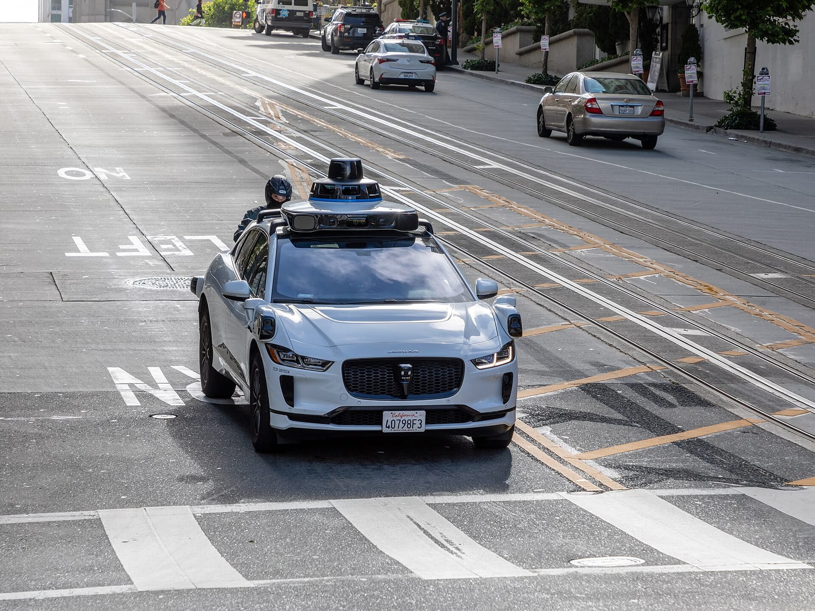 A driverless Waymo vehicle with roof sensors crossing California Street in San Francisco