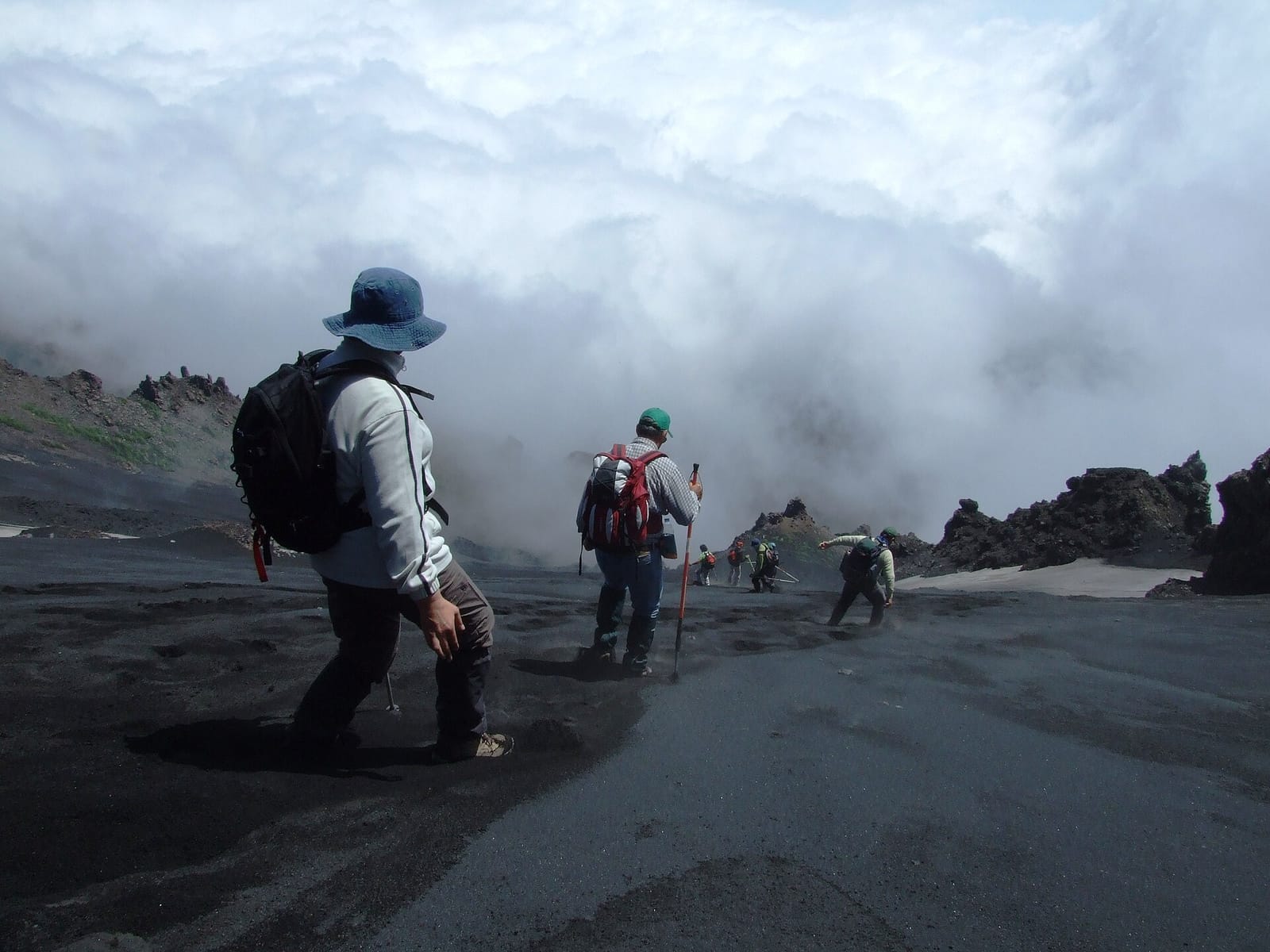 Hikers walking down a steep, misty volcanic slope on Mount Etna