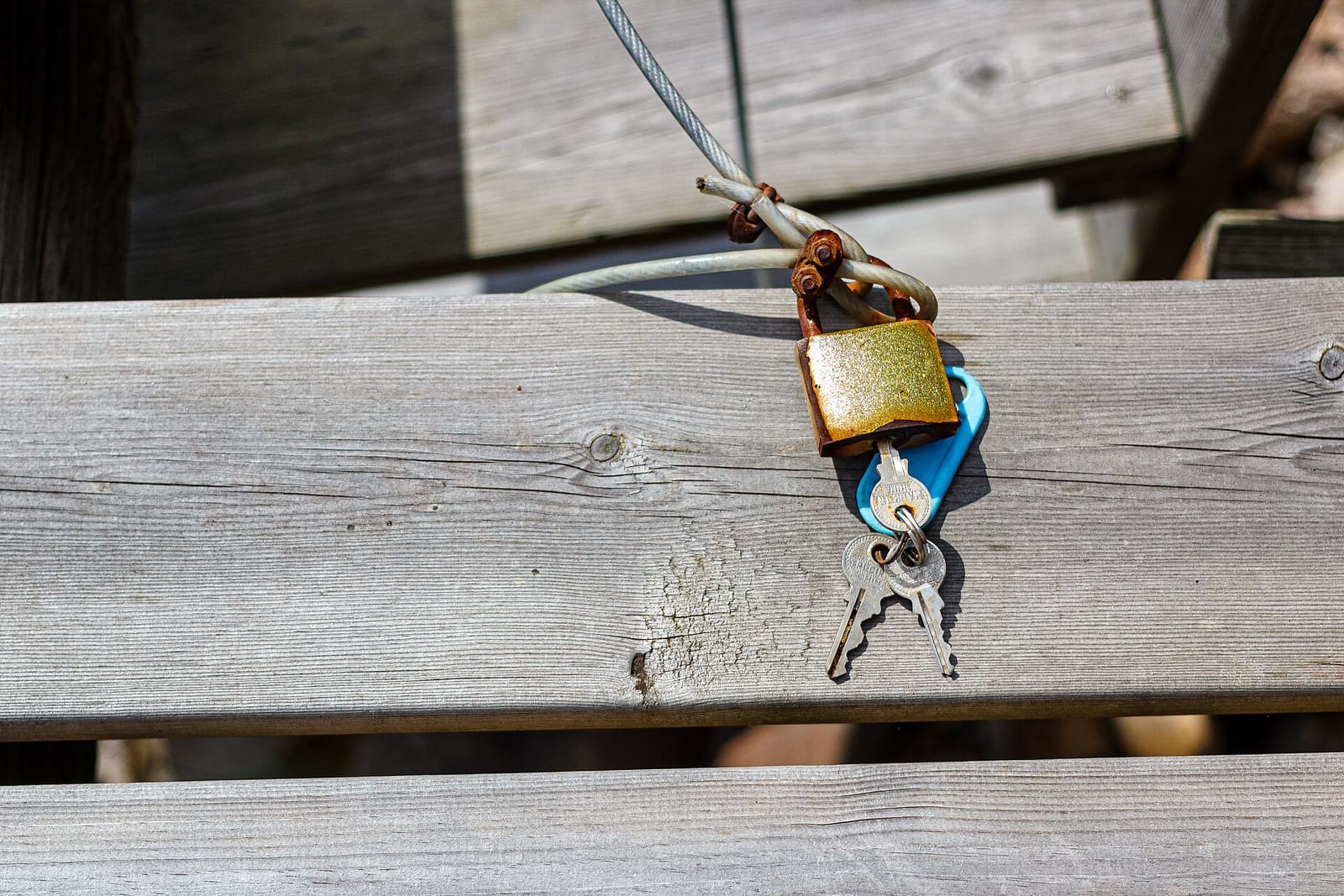 Small brass padlock with keys hanging from a wooden railing