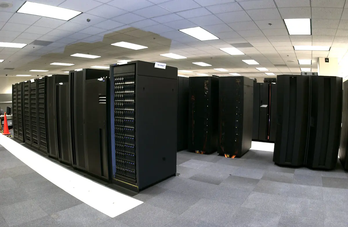 Rows of black IBM supercomputer cabinets in a machine room with a raised white floor