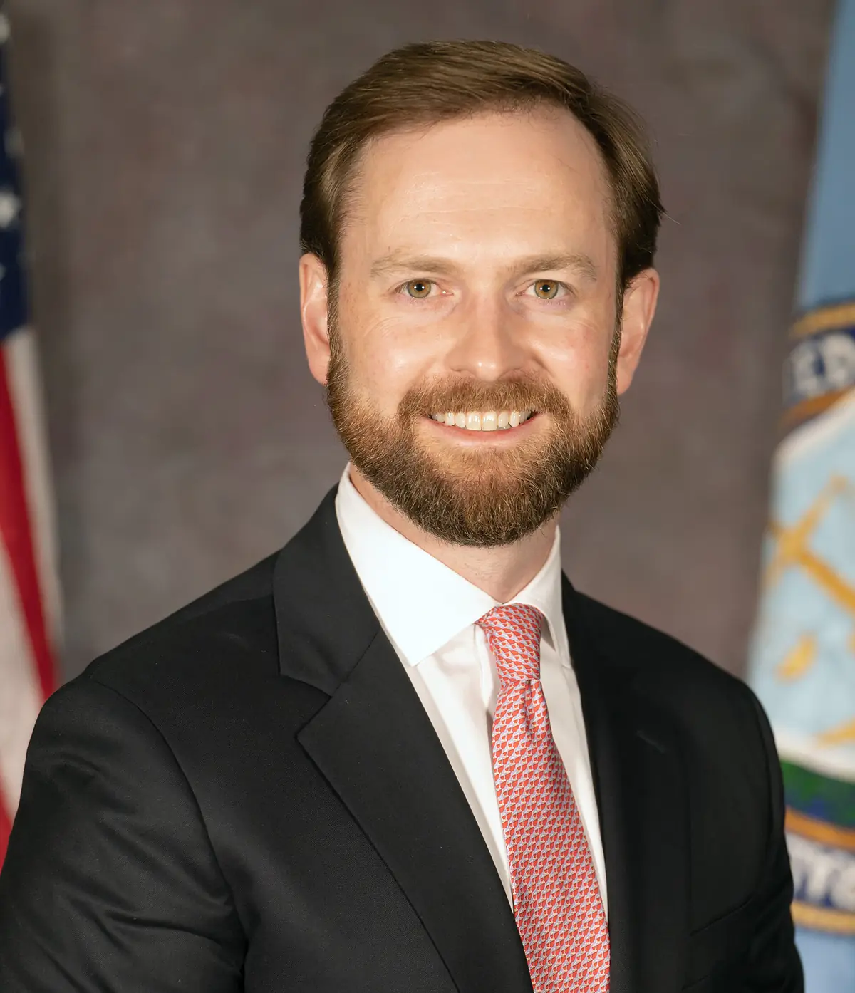 Official portrait of Andrew Ferguson in a dark suit and red tie in front of flags