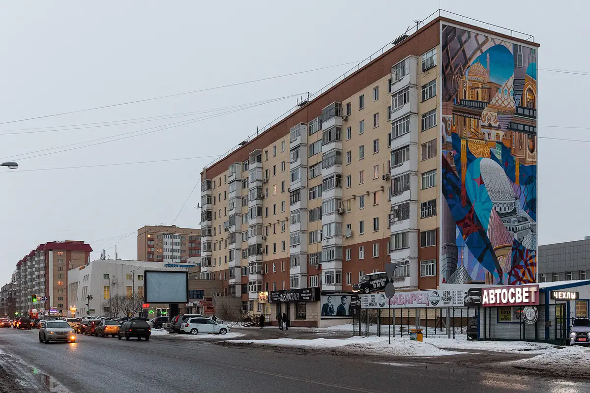 A wide street in Astana in February with snow along the kerbs, slush on the road and apartment blocks on one side