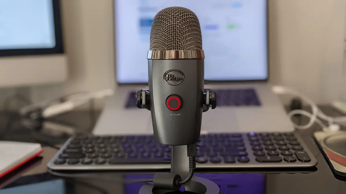 A microphone in front of a blurred keyboard and laptop in a home office