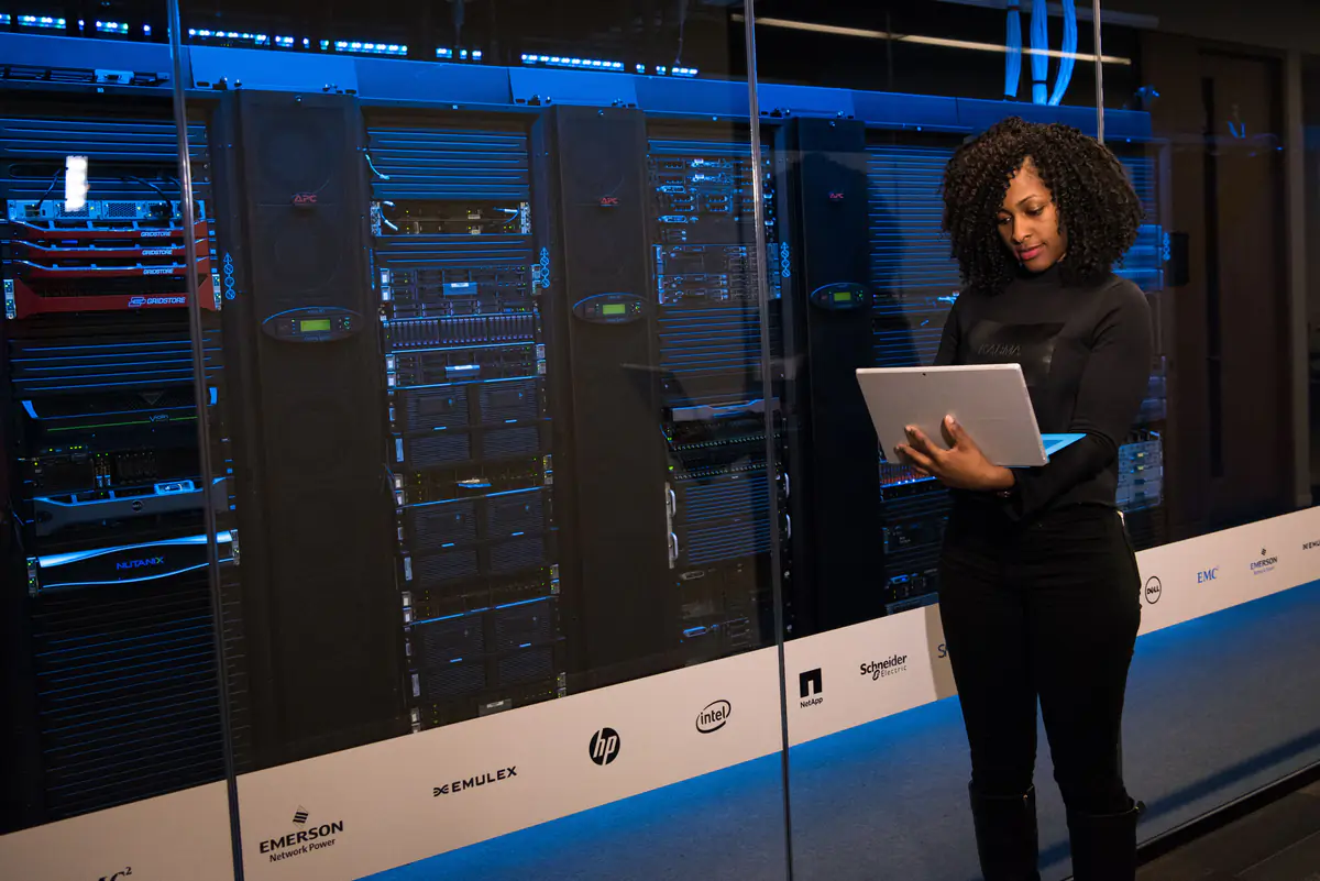 An engineer using a laptop beside rows of server racks