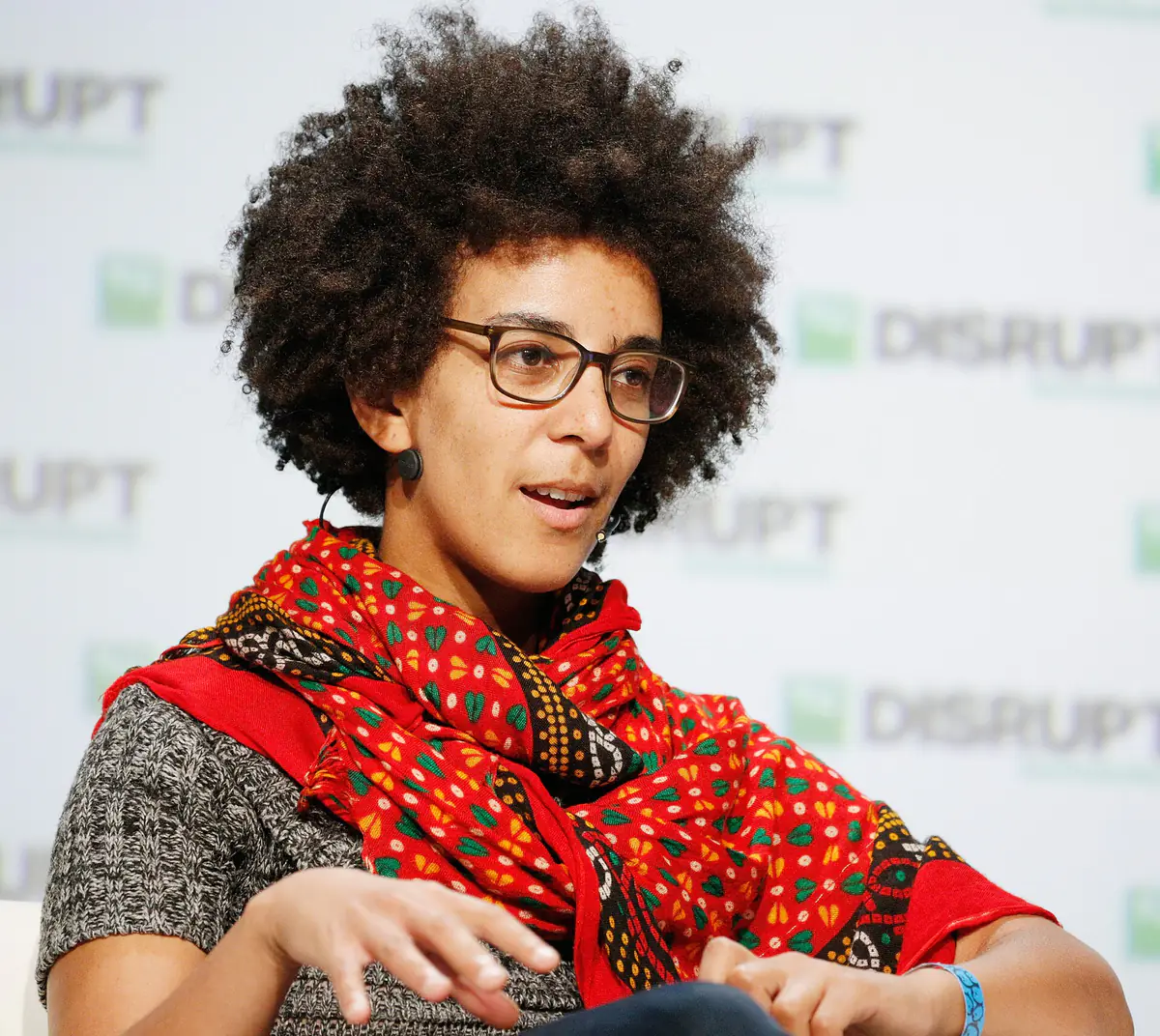 Timnit Gebru, wearing glasses and a red patterned scarf, speaking on stage